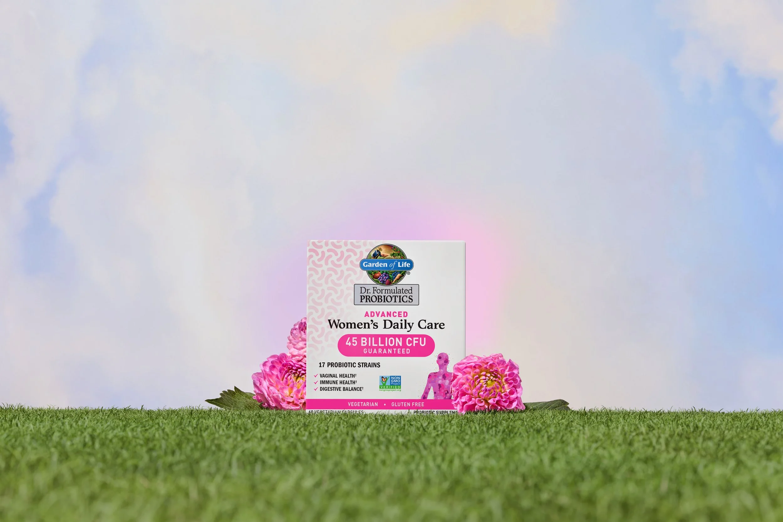 Box of Garden of Life Dr. Formulated Probiotics Women's Daily Care, advanced formula with 17 probiotic strains, guaranteed 45 billion CFU, vegetarian and gluten free, placed on a grassy surface with pink flowers and a partly cloudy sky background.