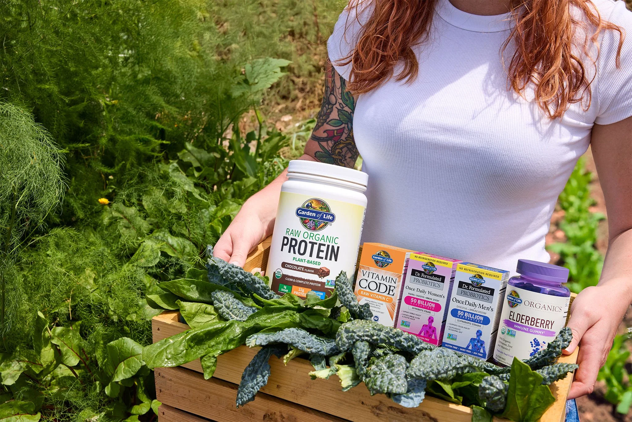Person holding a wooden crate containing health supplements and herbal leaves, outdoors in a garden.