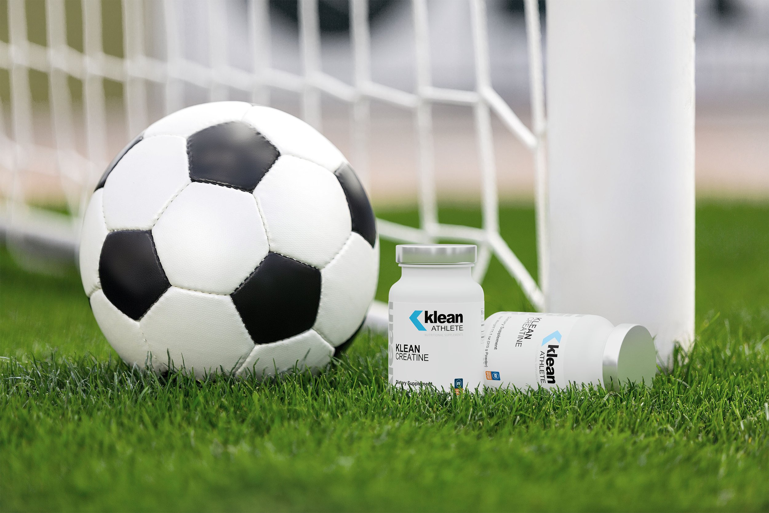 Soccer ball and dietary supplement bottles on grass field near goalpost.