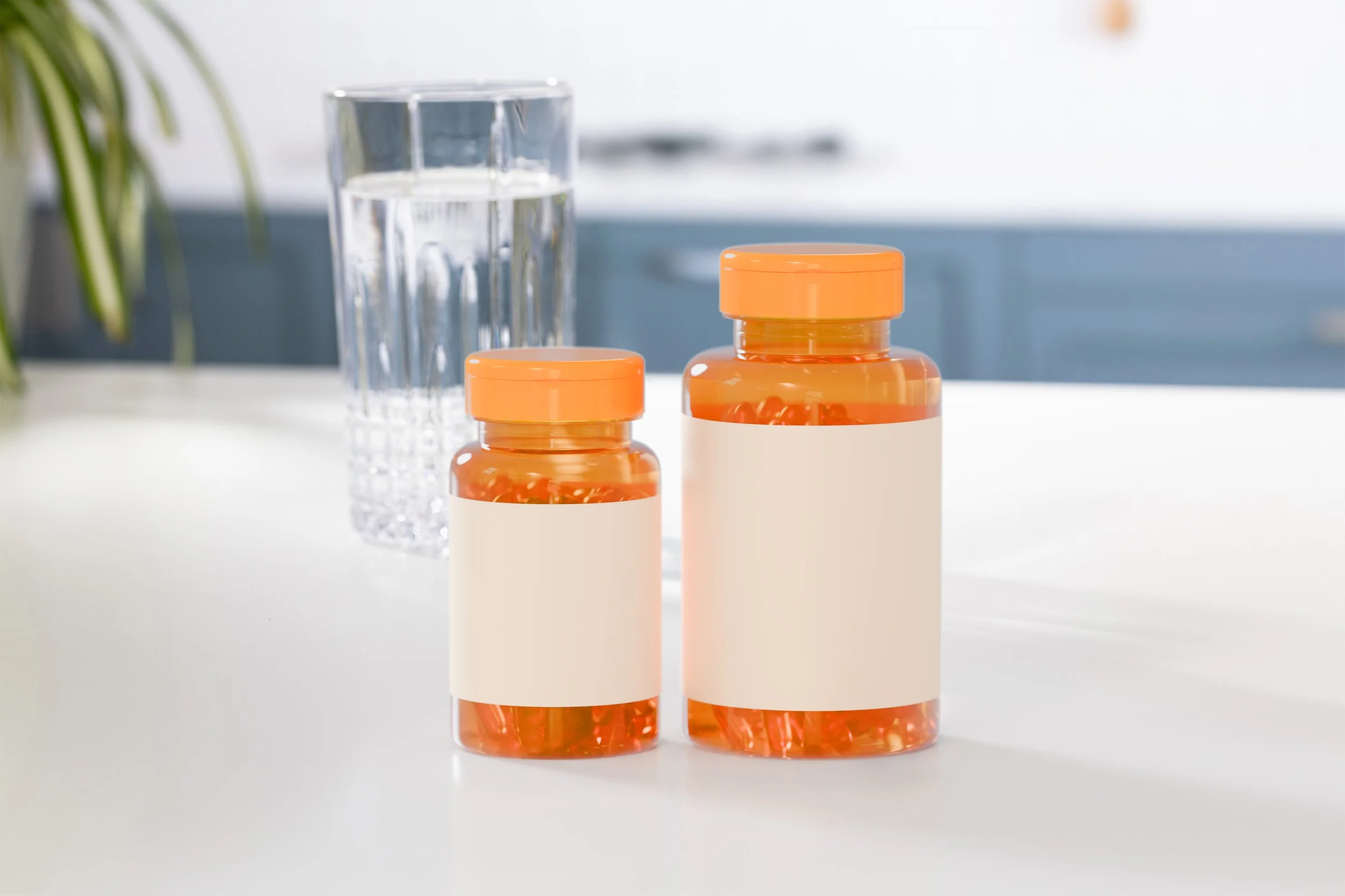 Two orange pill bottles with blank labels on a white surface, with a glass of water and a blurred kitchen background.