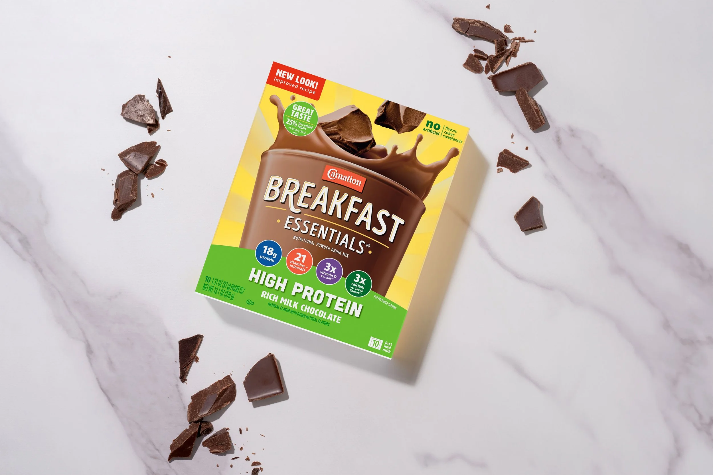 A box of Carnation Breakfast Essentials high protein rich milk chocolate nutritional powder drink mix on a white marble surface, surrounded by broken pieces of chocolate.