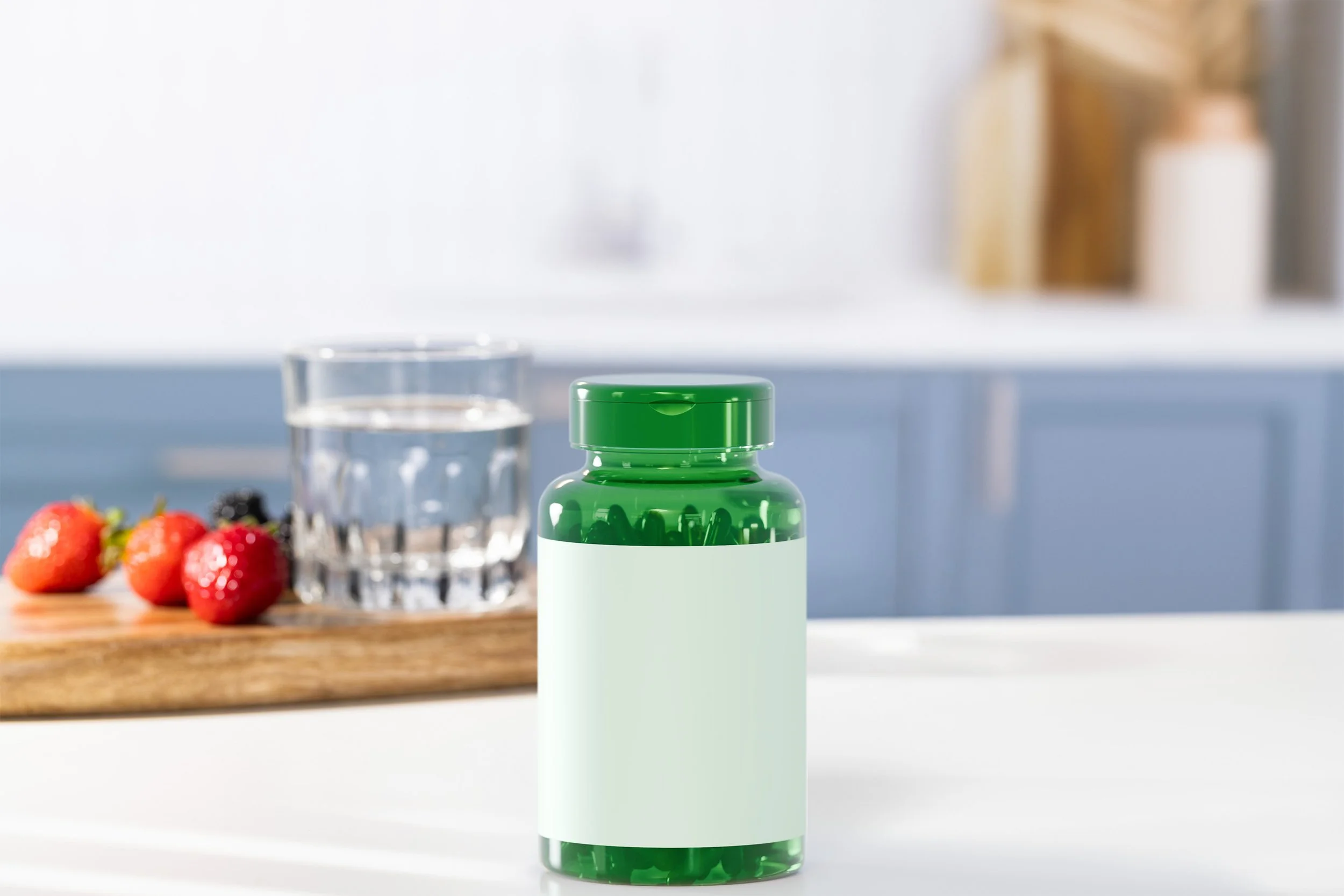 Green supplement bottle with blank white label on white countertop, blurred glass of water and strawberries in background in a kitchen.