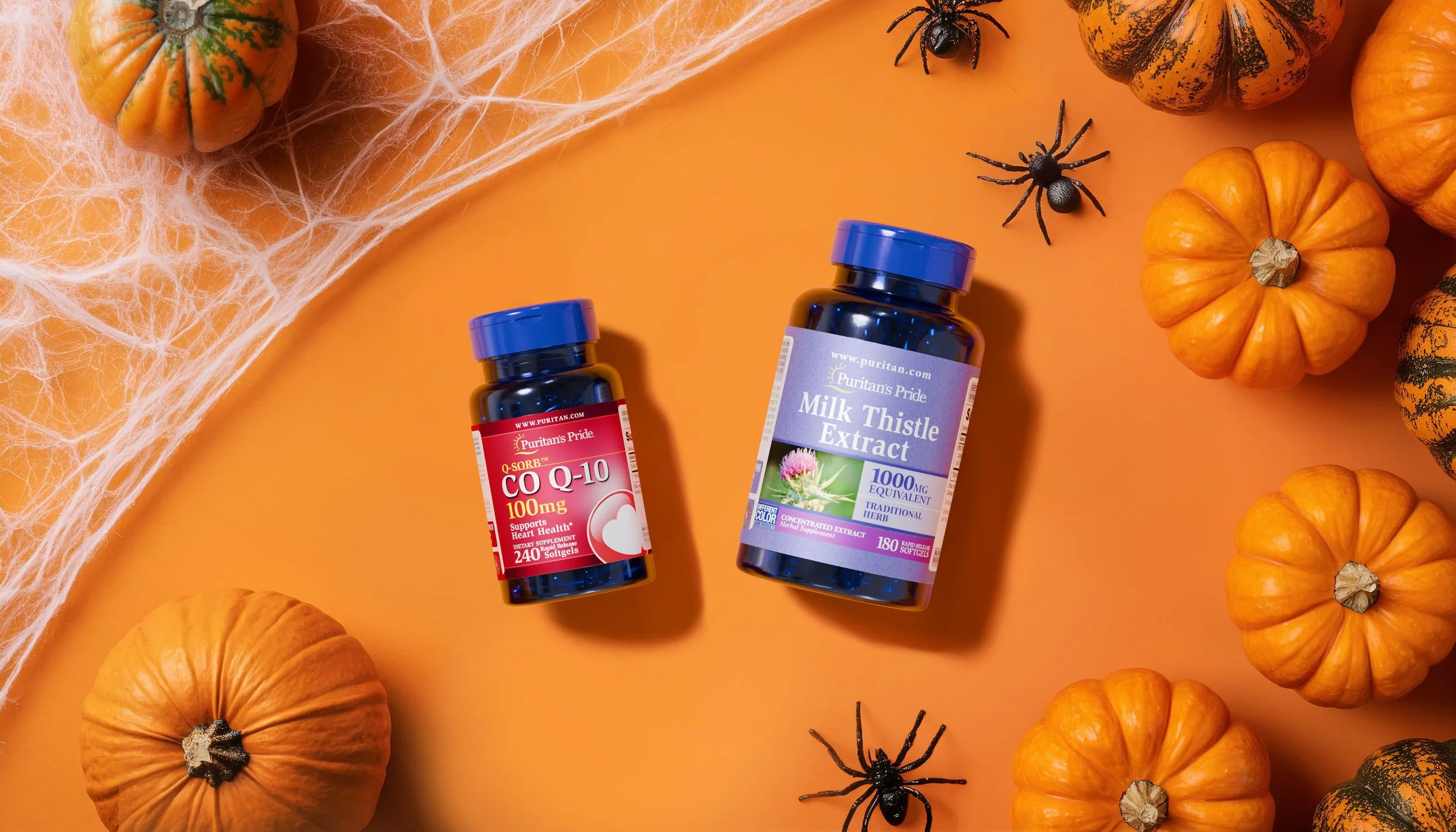Two bottles of dietary supplements, one labeled 'CO Q-10 100mg' and the other 'Milk Thistle Extract,' are placed on an orange background surrounded by small pumpkins, black plastic spiders, and faux cobwebs.