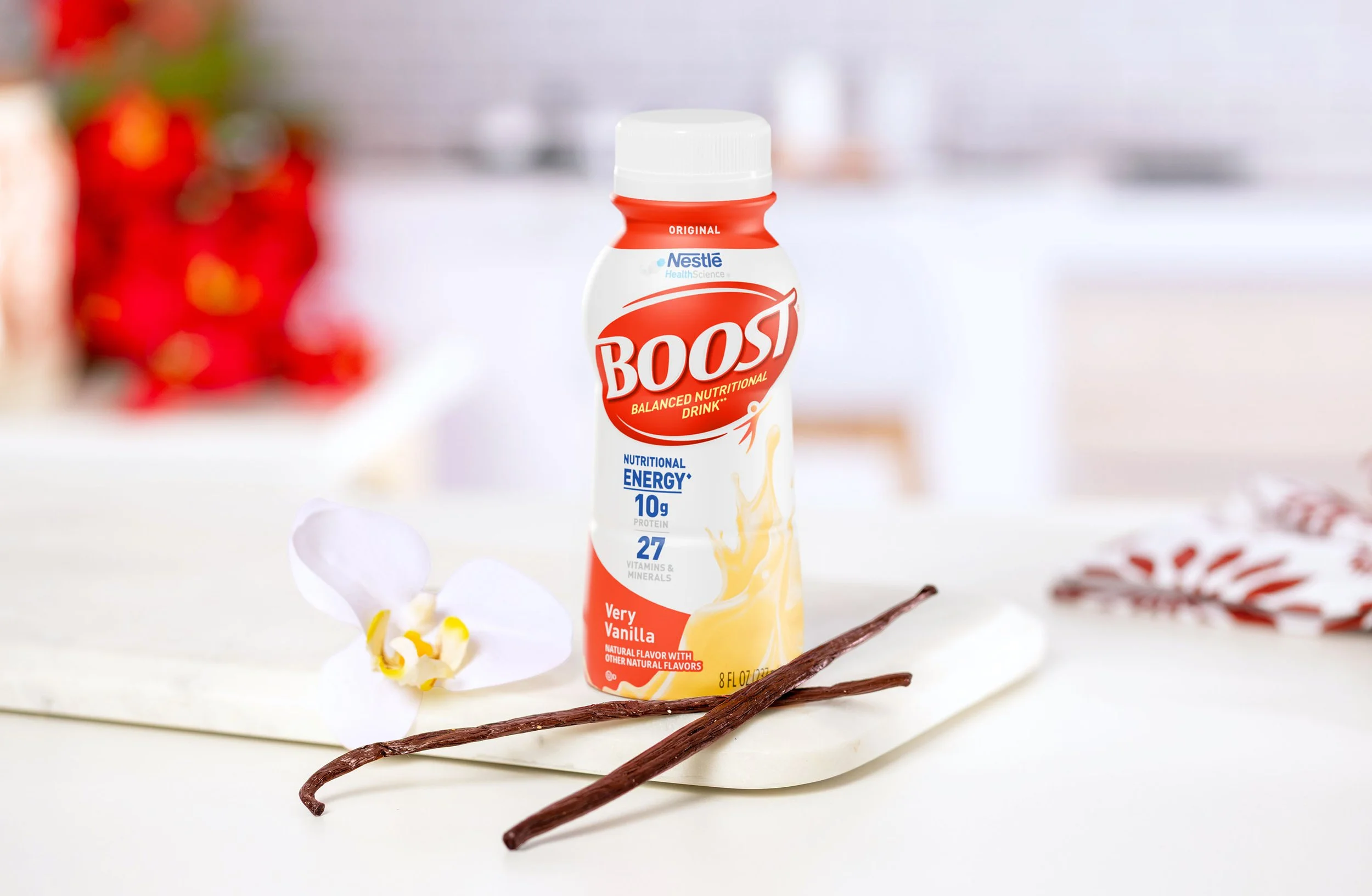 A bottle of Boost Very Vanilla nutritional drink placed on a white marble surface with vanilla beans and a white flower nearby.