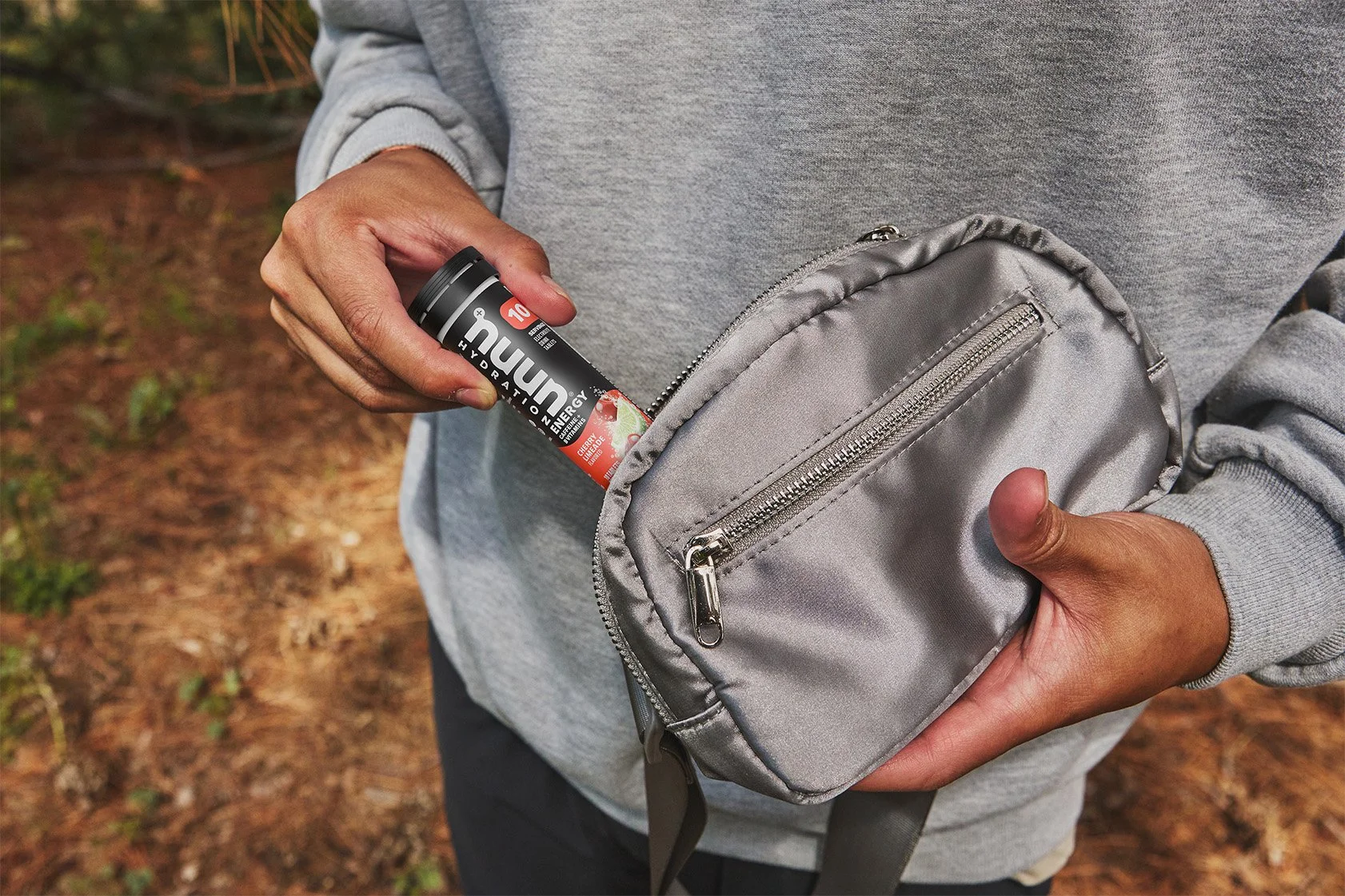 A person placing a Nuun hydration tablet into a gray backpack in an outdoor setting.