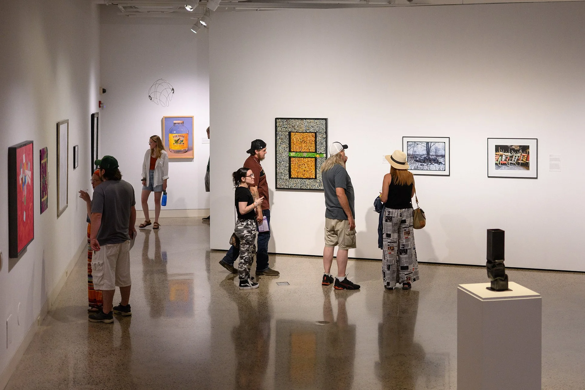 Visitors viewing artwork in a contemporary art gallery with framed pieces displayed along white walls.