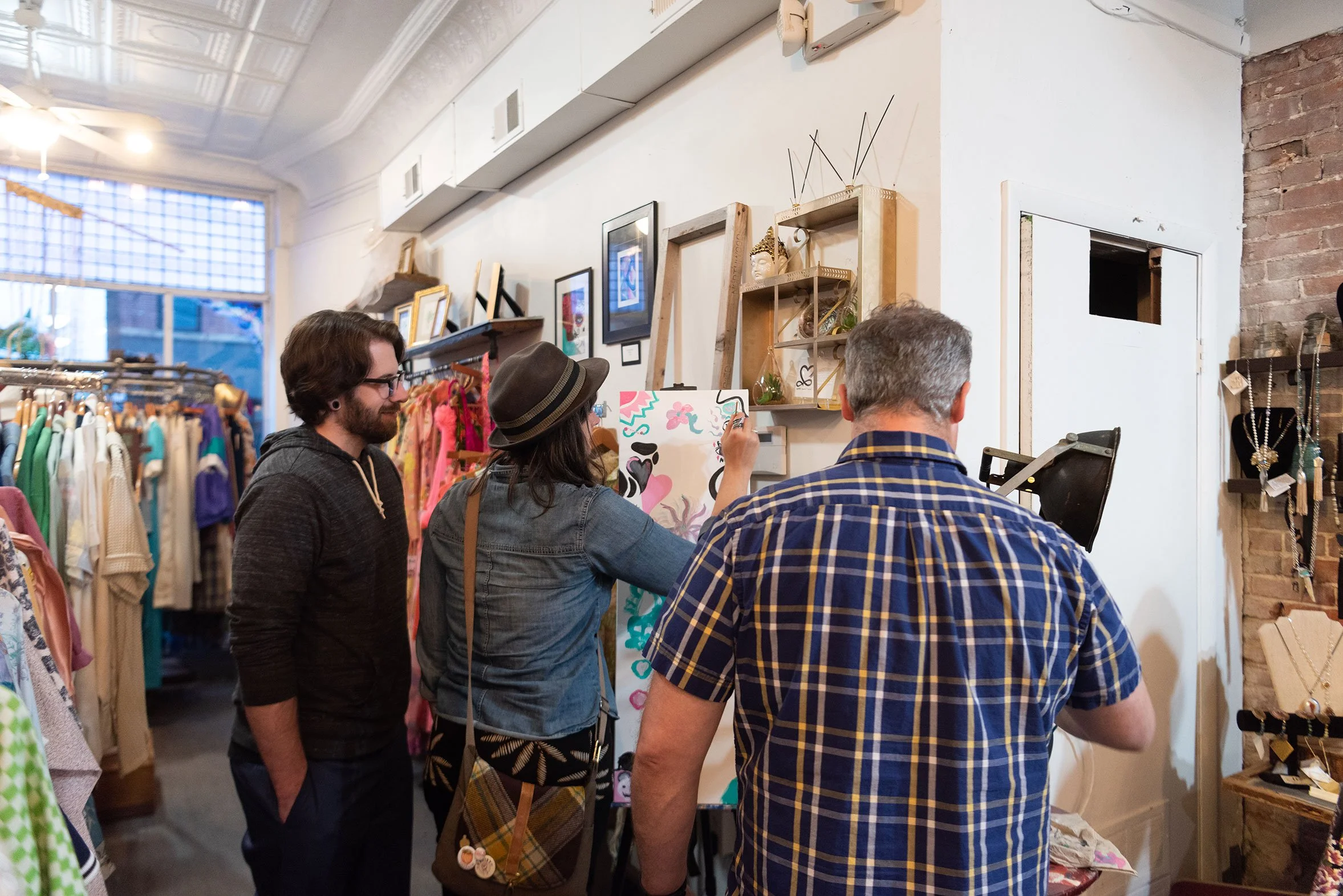 Visitors watching an artist paint during a pop-up gallery event inside a boutique space.
