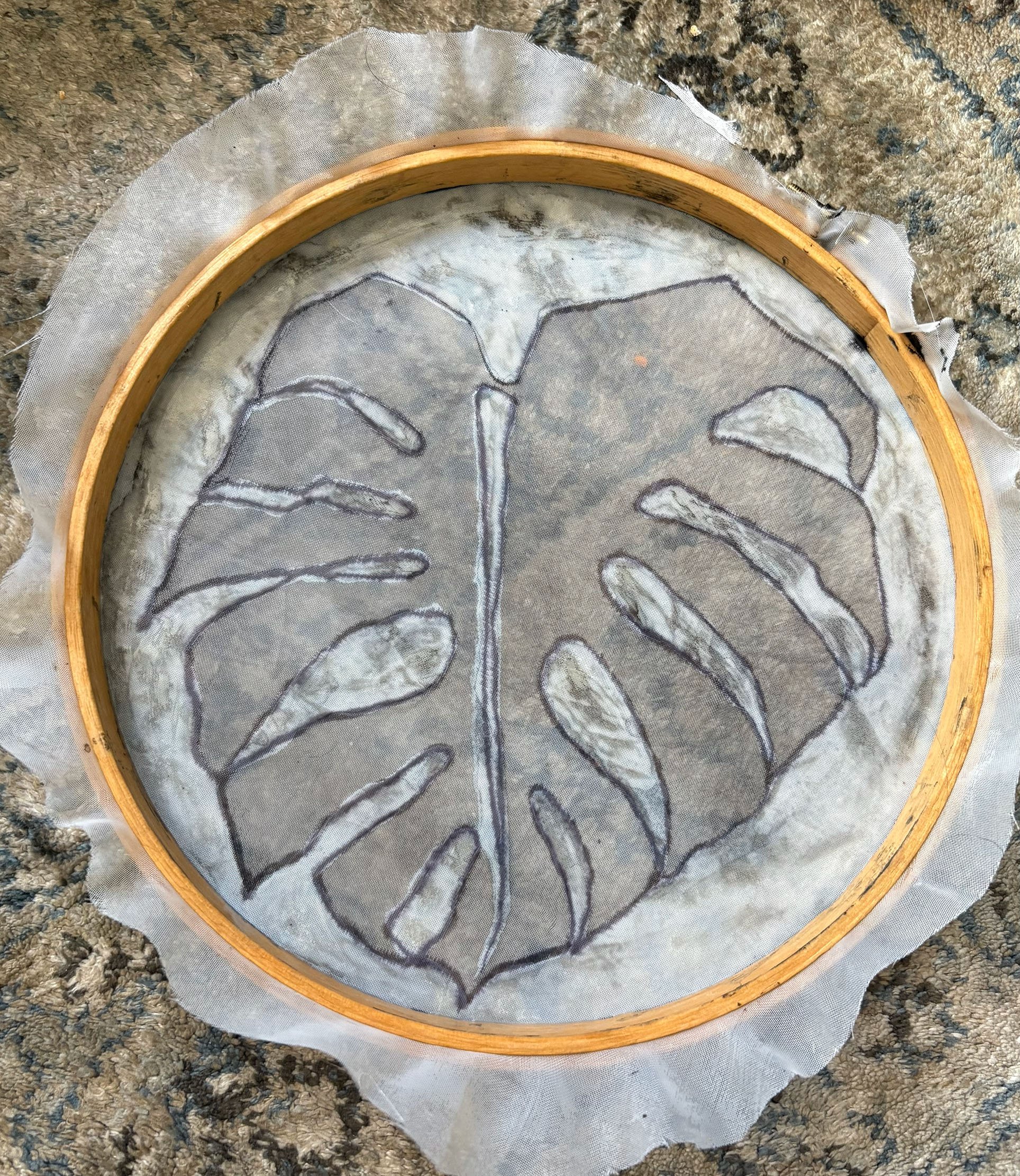A leaf design outline stitched on fabric, secured in a wooden embroidery hoop, placed on a textured surface.