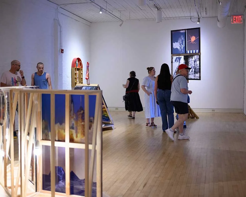 Visitors viewing artwork inside a contemporary gallery space with wooden floors, framed installations, and illuminated exhibits.