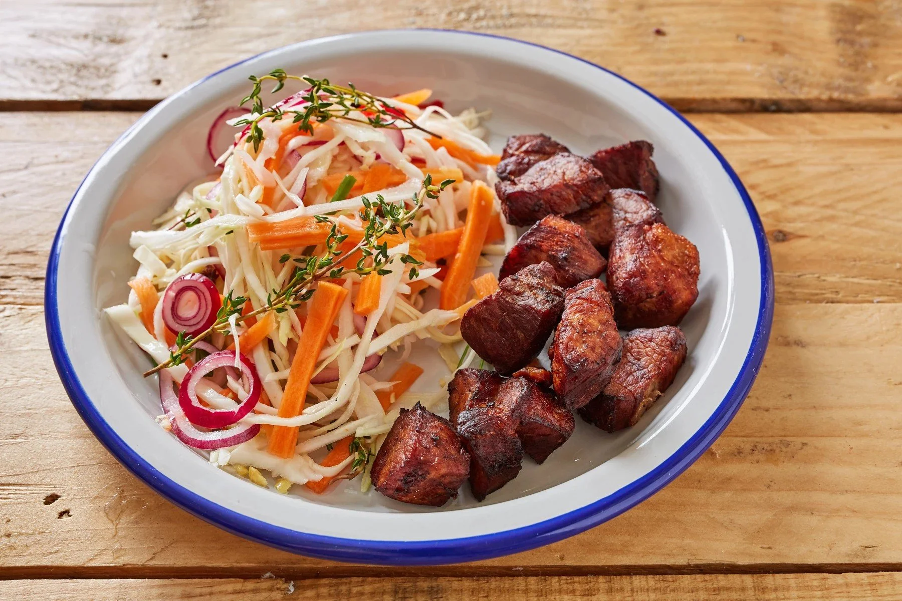 Haitian fried pork served beside cabbage, carrot, and red onion pikliz on a white plate with a blue rim