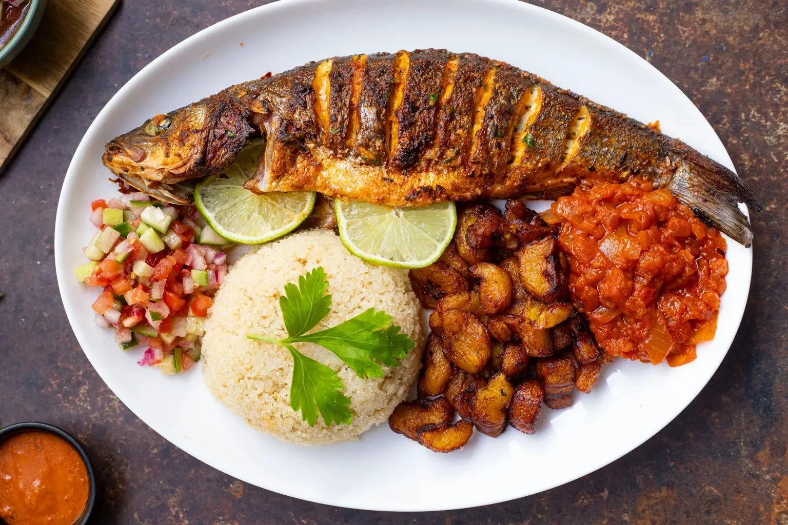 Whole grilled fish served with attiéké, fried plantains, tomato-onion sauce, and fresh salad