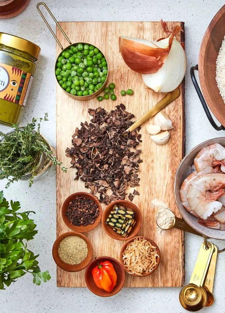 Ingredients for Haitian diri djon djon, including rice, black trumpet mushrooms, epís, herbs, Scotch bonnet pepper, peas, garlic, and aromatics.