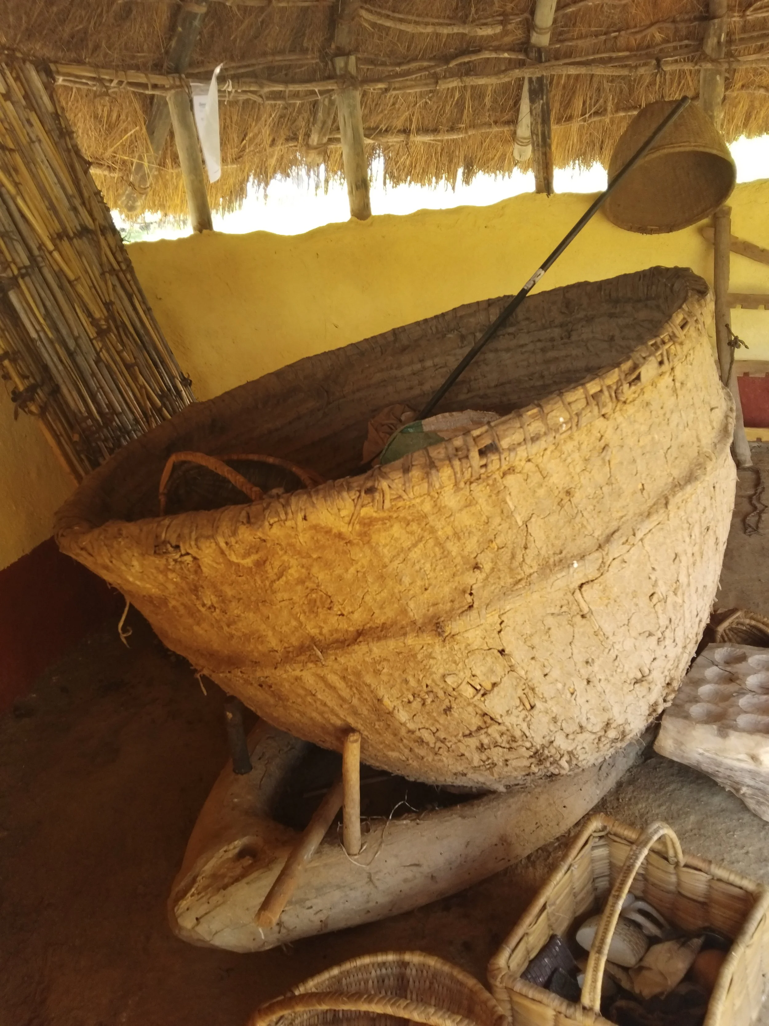 Large woven harvesting basket displayed indoors among other traditional implements