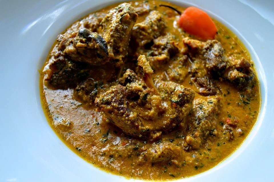 Bowl of thick golden-brown miyan gyada with assorted meat and a whole red pepper