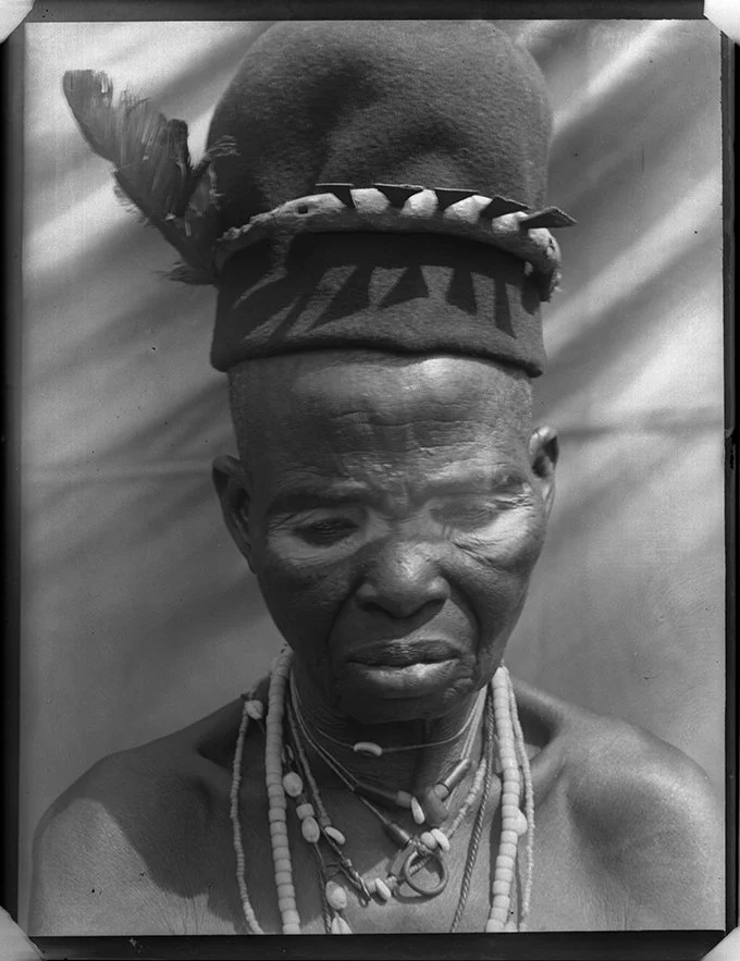 Portrait of the Omu of Okpanam wearing a feathered headdress and white chalk markings in 1912