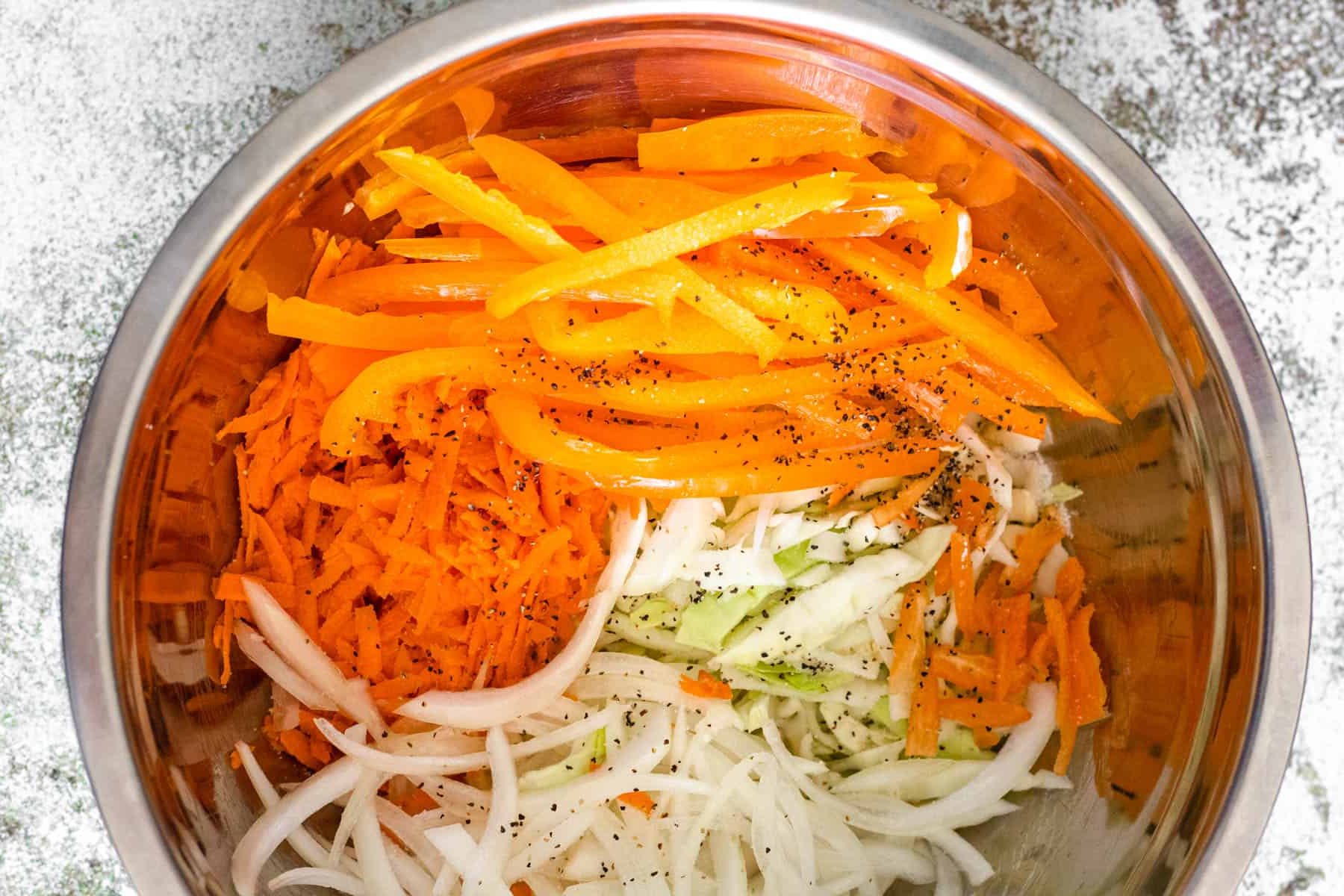 Shredded cabbage, grated carrot, sliced onion, and bell pepper seasoned in a bowl for pikliz