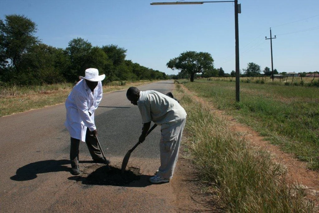 Two men using shovels to fill a pothole on a road in Bulawayo, Zimbabwe