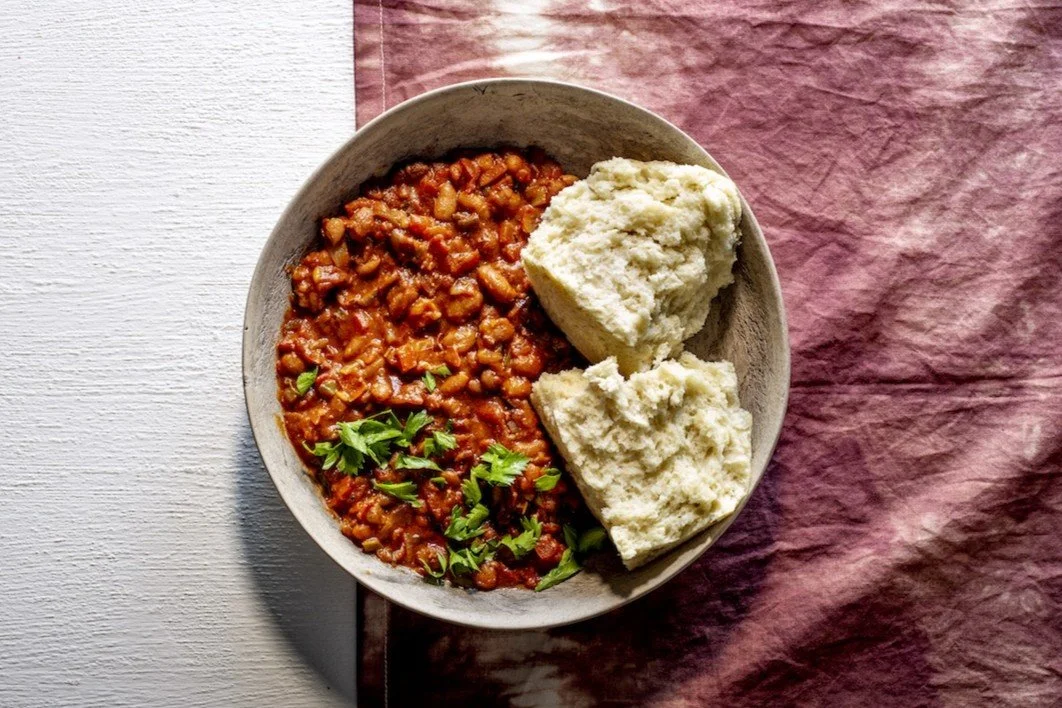 Pieces of South African steamed bread, ujeqe, served alongside a rich tomato-based sugar bean stew known as ubhonsisi.