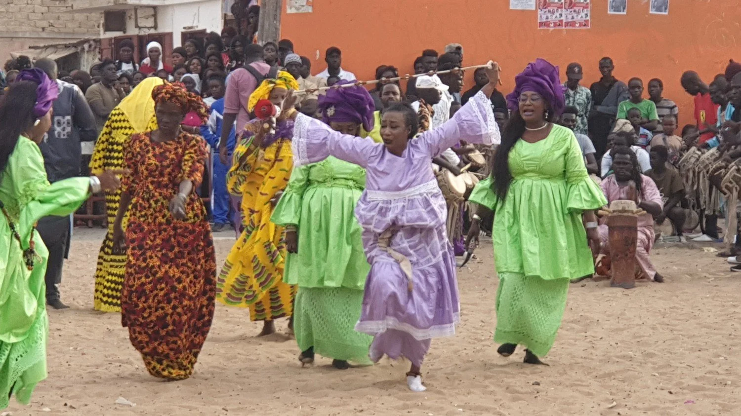 Women dancing in a Dakar street while musicians play Senegalese sabar drums behind them