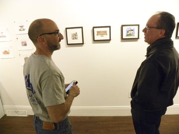 Alex talks with a visitor while standing in front a row of his artwork