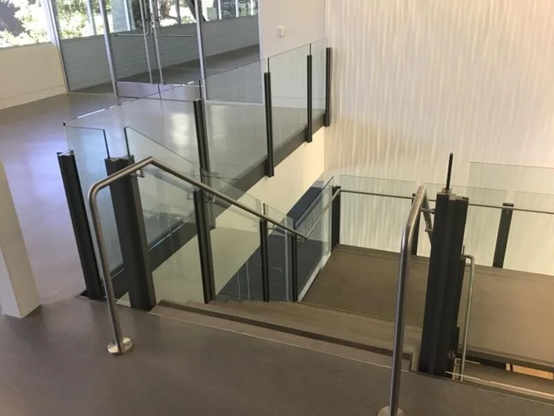 Indoor staircase with glass railings and metal handrails, leading to a lower level in a modern building.