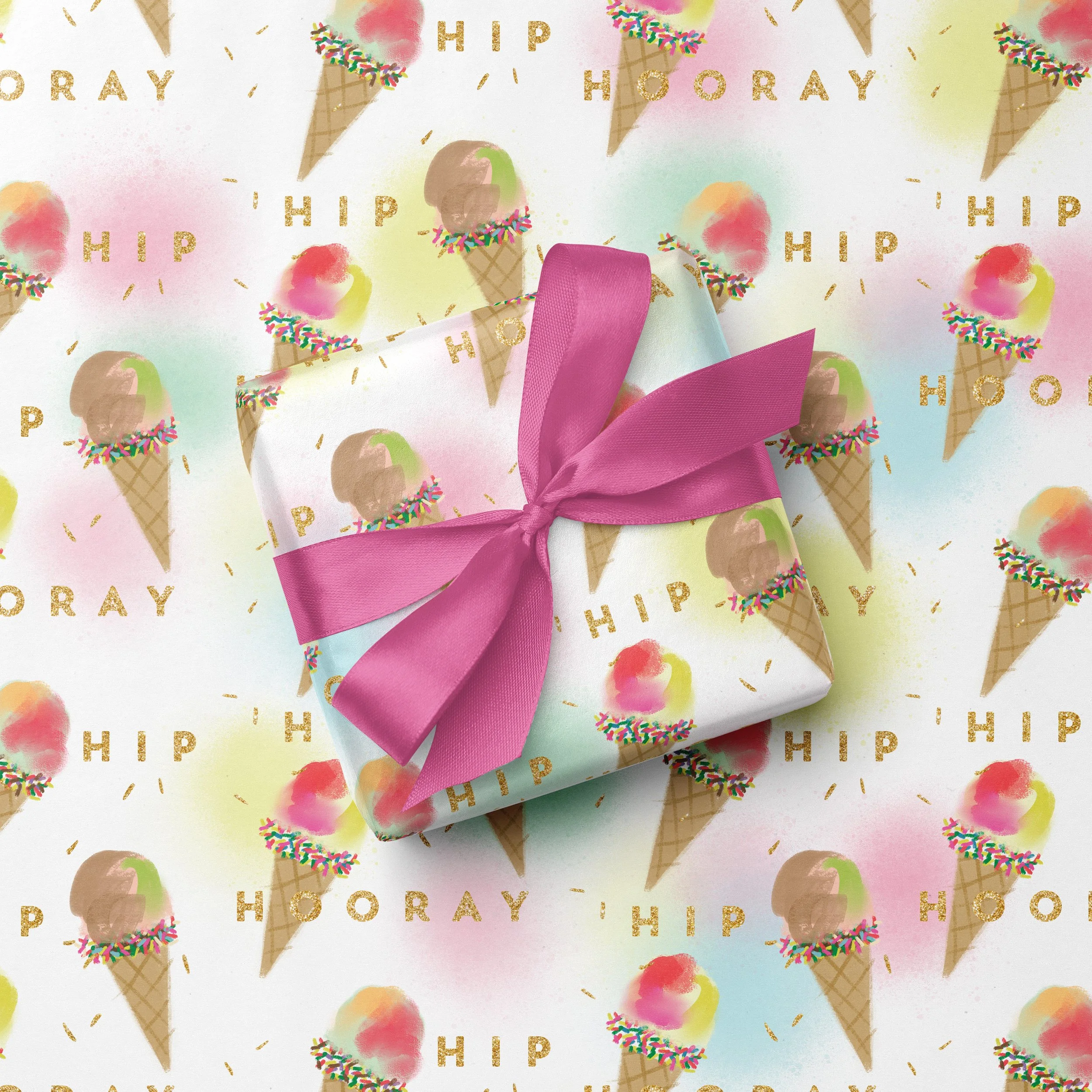 A wrapped gift box with pink ribbon on pastel-colored wrapping paper featuring ice cream cones and the words "HIP HOORAY" in gold lettering and colorful sprinkles.