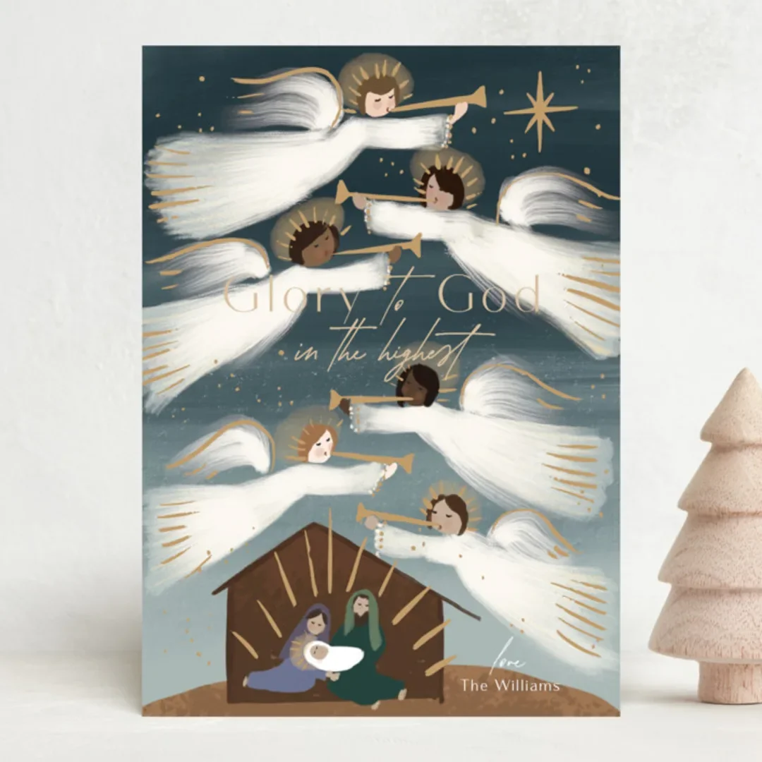Christmas greeting card featuring angels playing trumpets above nativity scene with Mary, Joseph, and baby Jesus in a manger. Text reads 'Glory to God in the highest.'