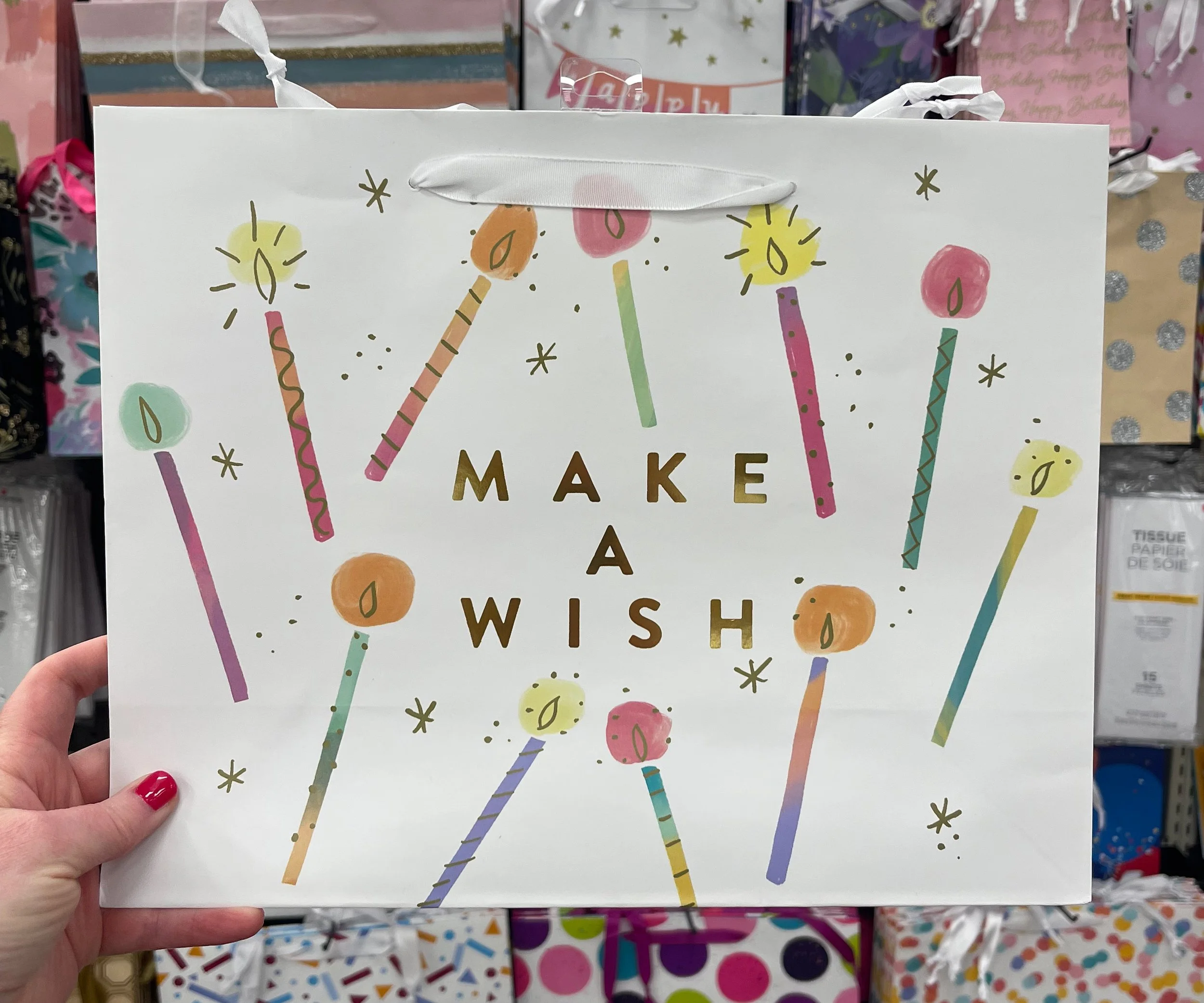 A white gift bag decorated with colorful birthday candles and the words 'Make a Wish' in gold letters.