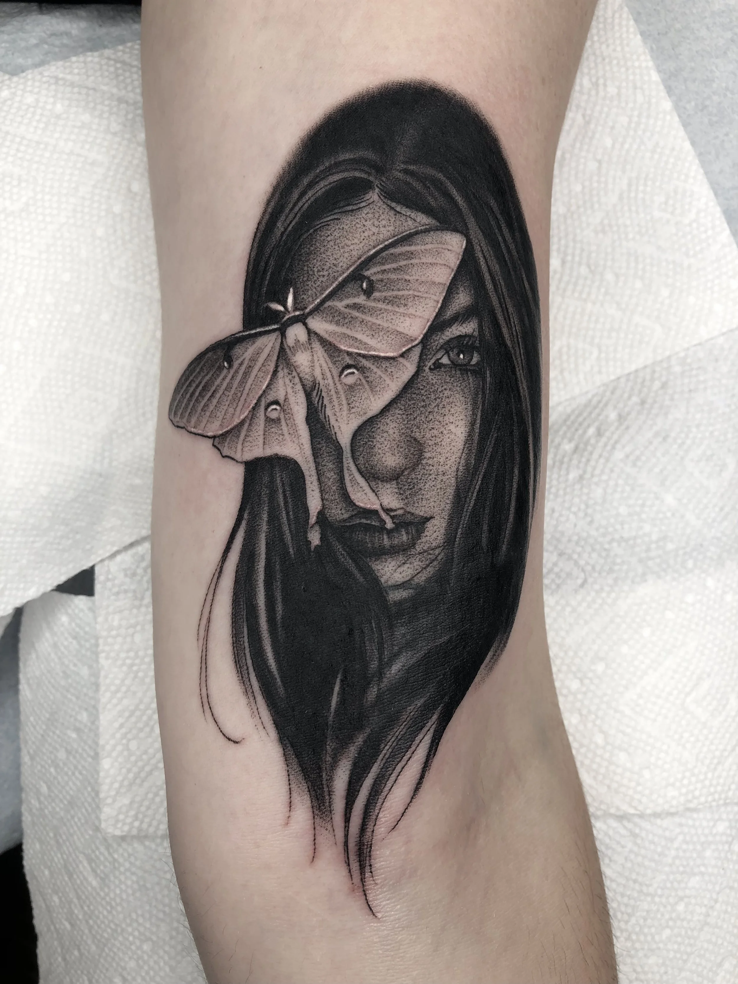 Black and gray tattoo of a woman with a butterfly covering part of her face on a person's arm.