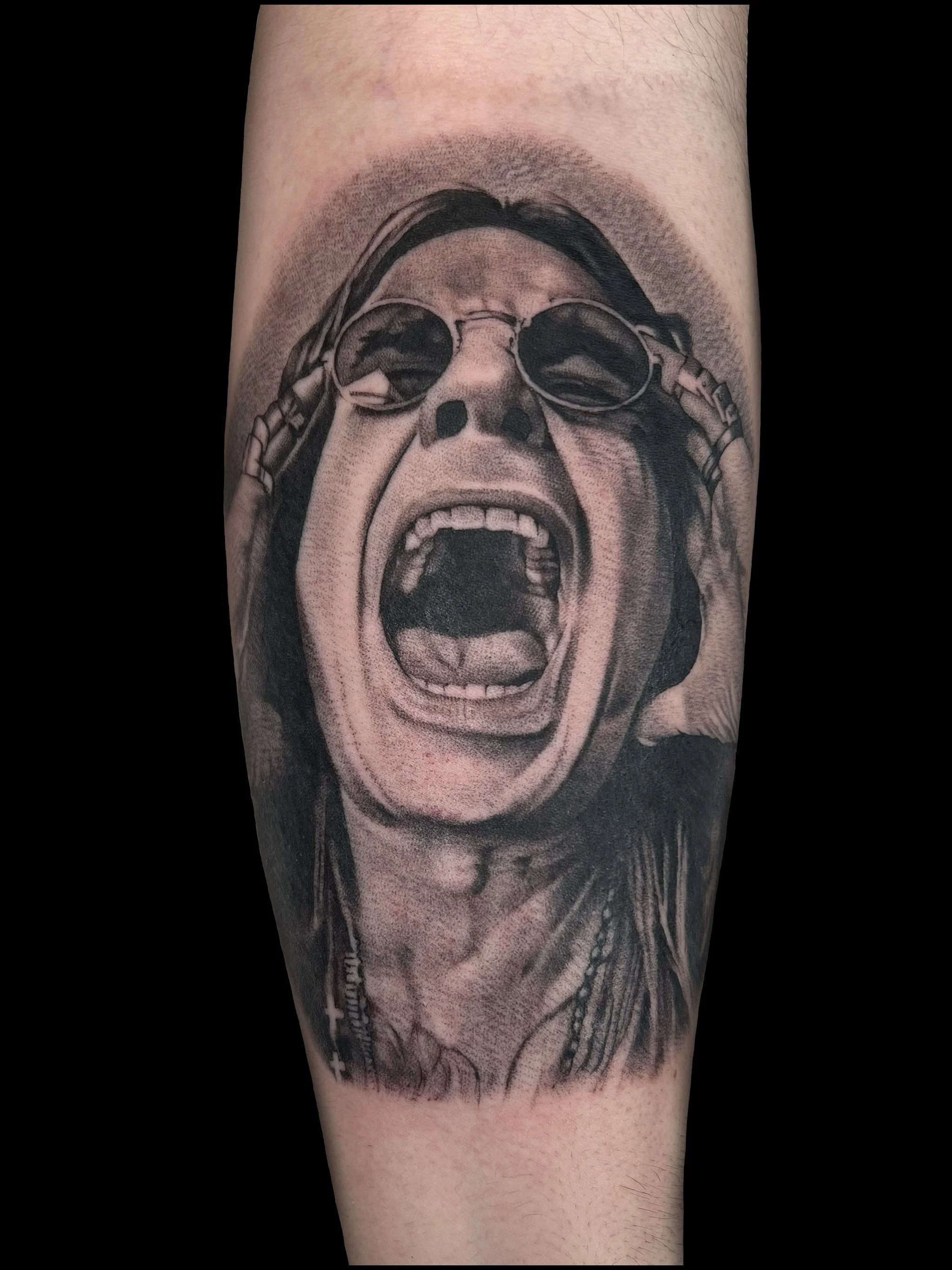 Black and gray tattoo of a woman screaming with sunglasses, with her mouth wide open and eyes closed, on a person's arm.