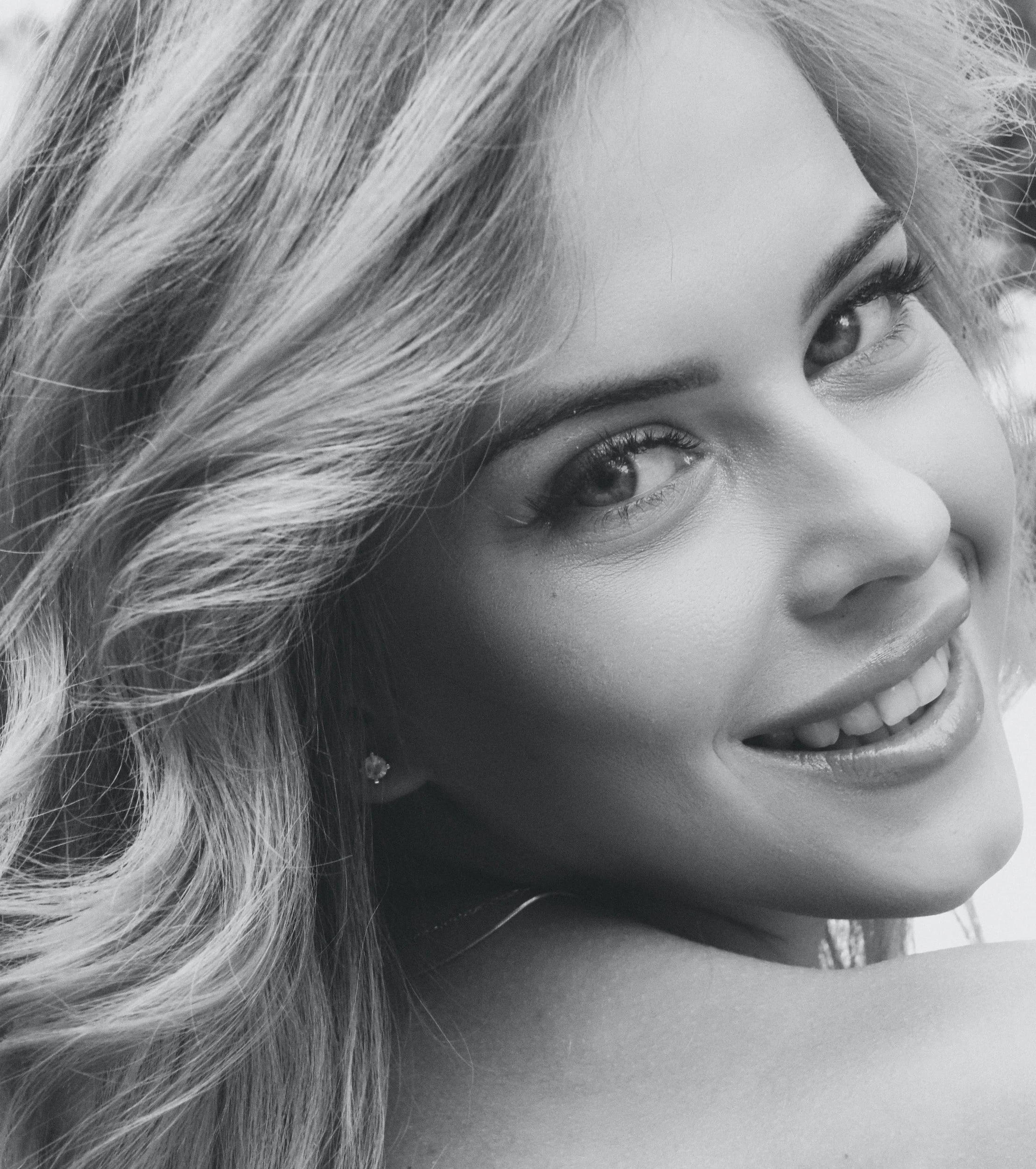 Close-up black and white portrait of a smiling woman with wavy hair and expressive eyes.