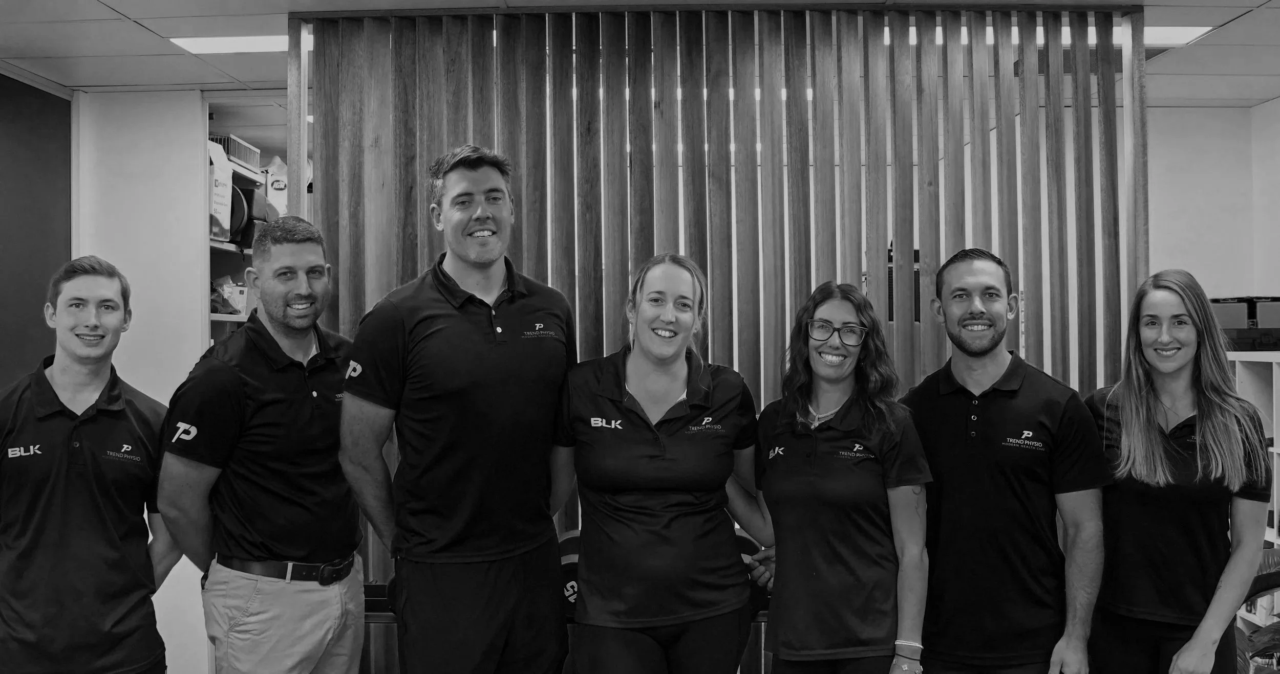 Team photo of seven people smiling, standing in a sports performance gym.