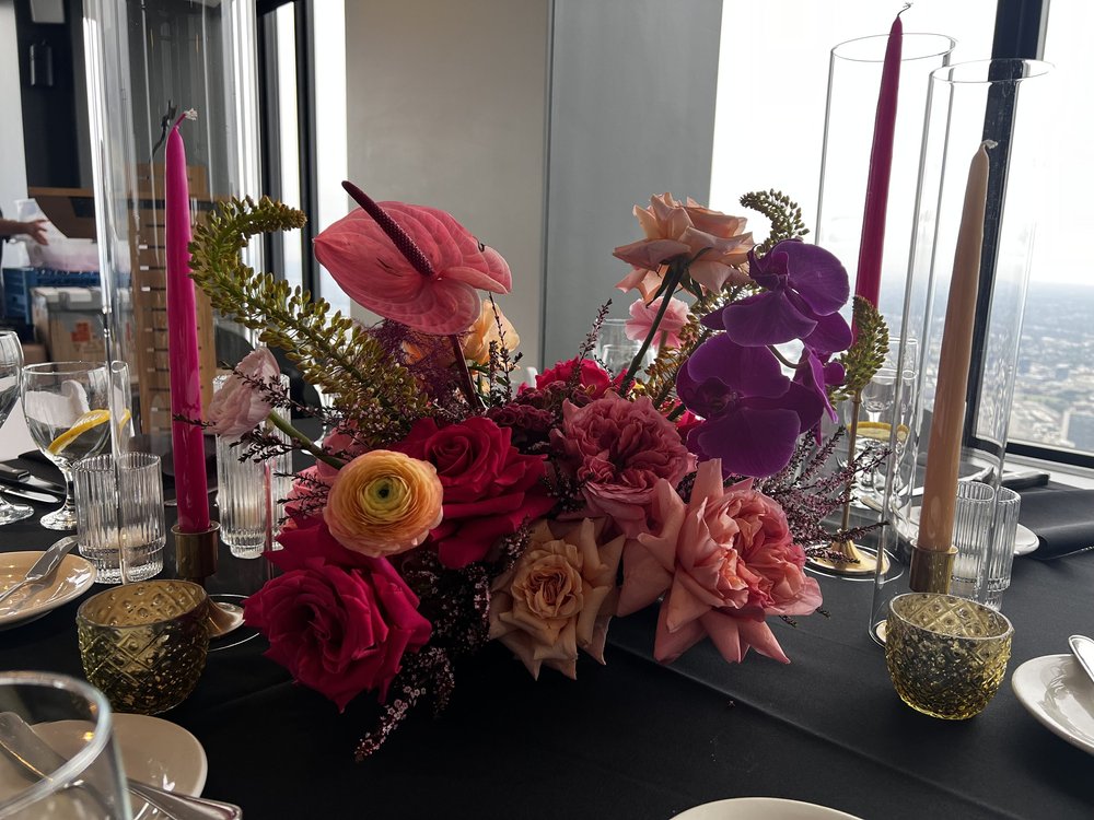 Rich pink and purple flowers with pink taper candles on a dark dinner table