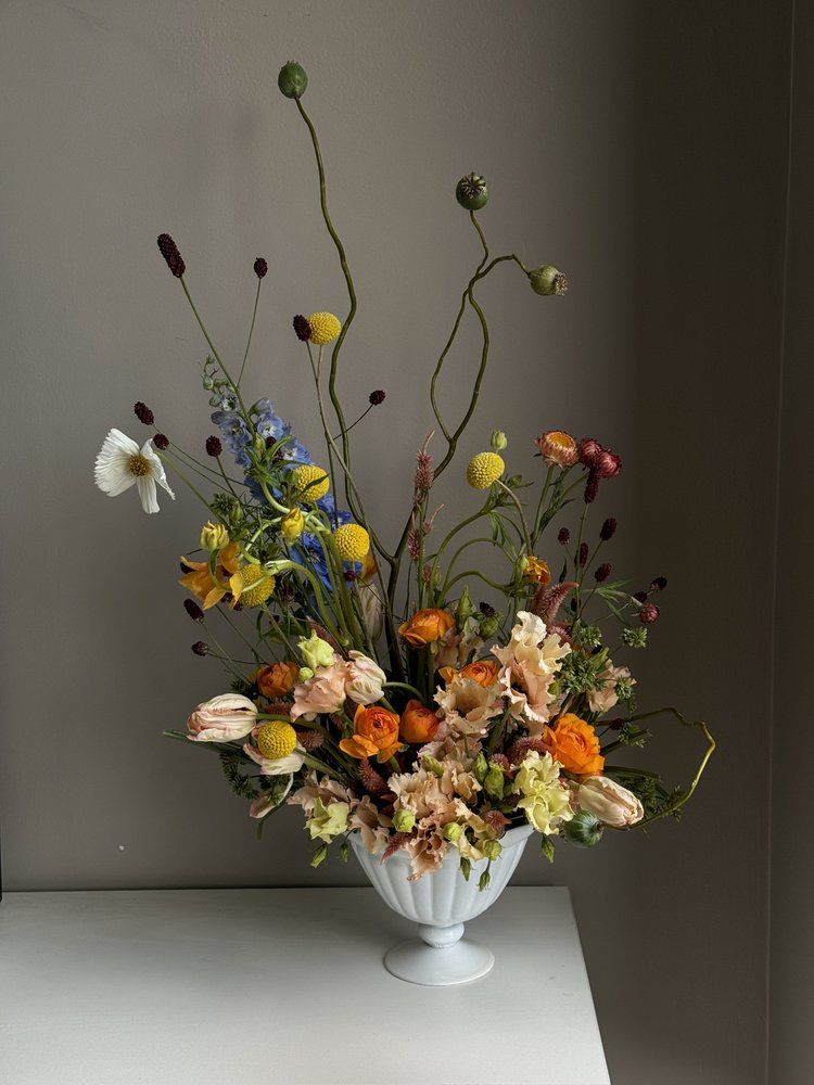 Airy statement flowers in peach, orange and blue on a white pedestal