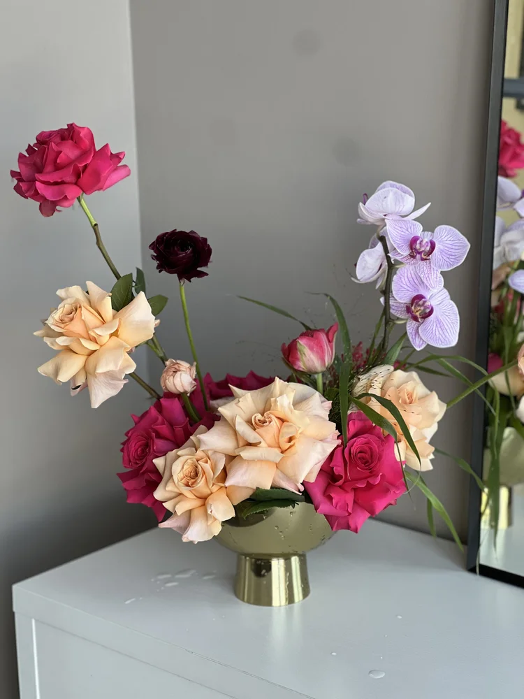 Peach and pink roses with purple orchids in a sculptural gold bowl