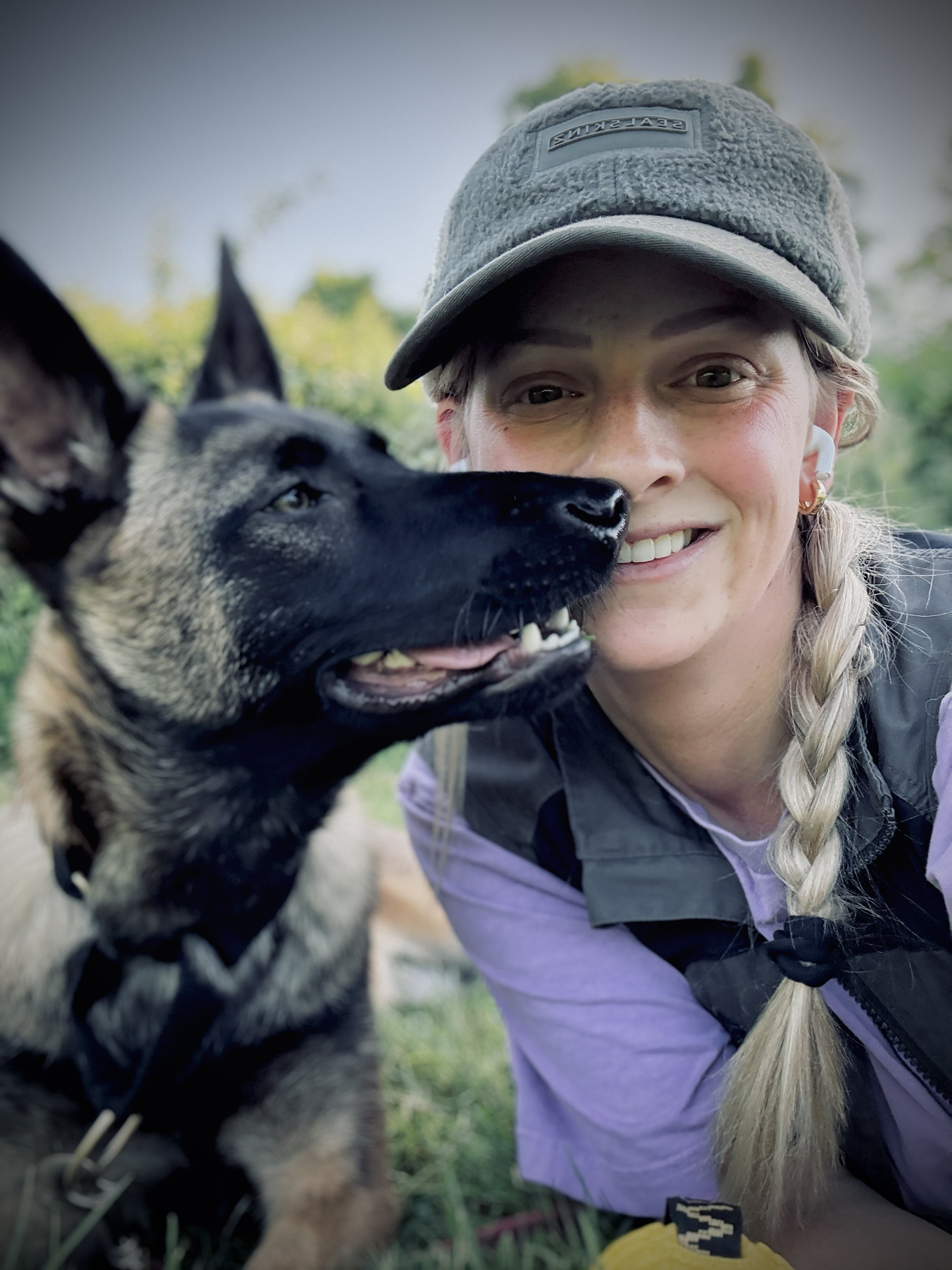 Sezan Oz Dog trainer dog behaviourist lying on the ground smiling  with her malinois close to her face.