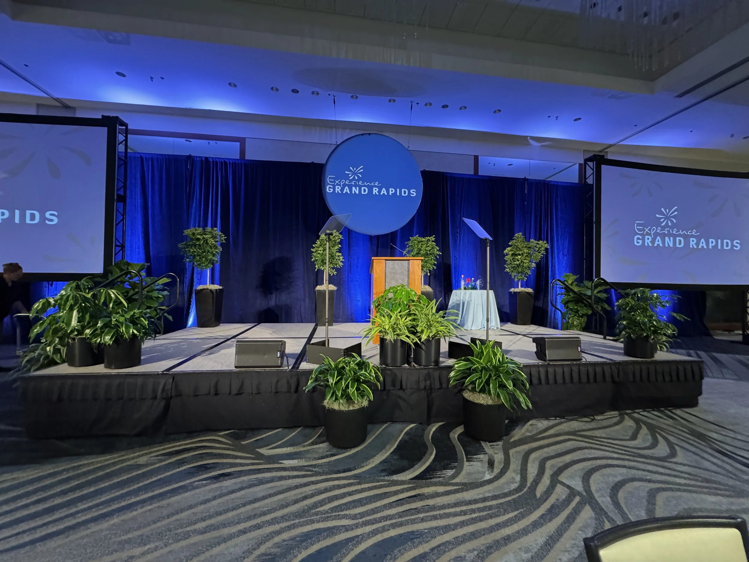 Potted plant rentals staged on an event stage with blue lighting.