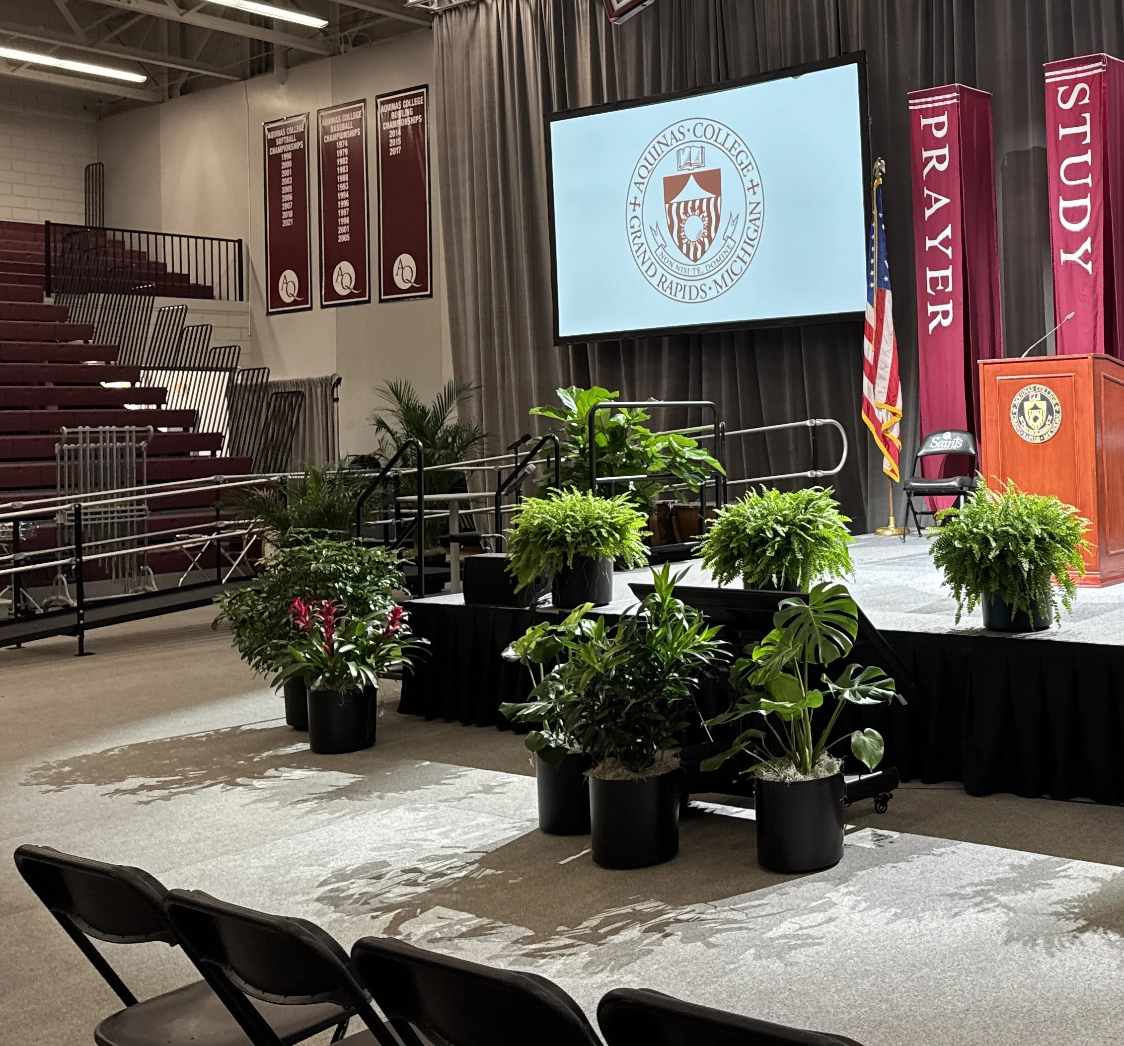 Ferns and tropical plants arranged on stage risers for an Aquinas College event.