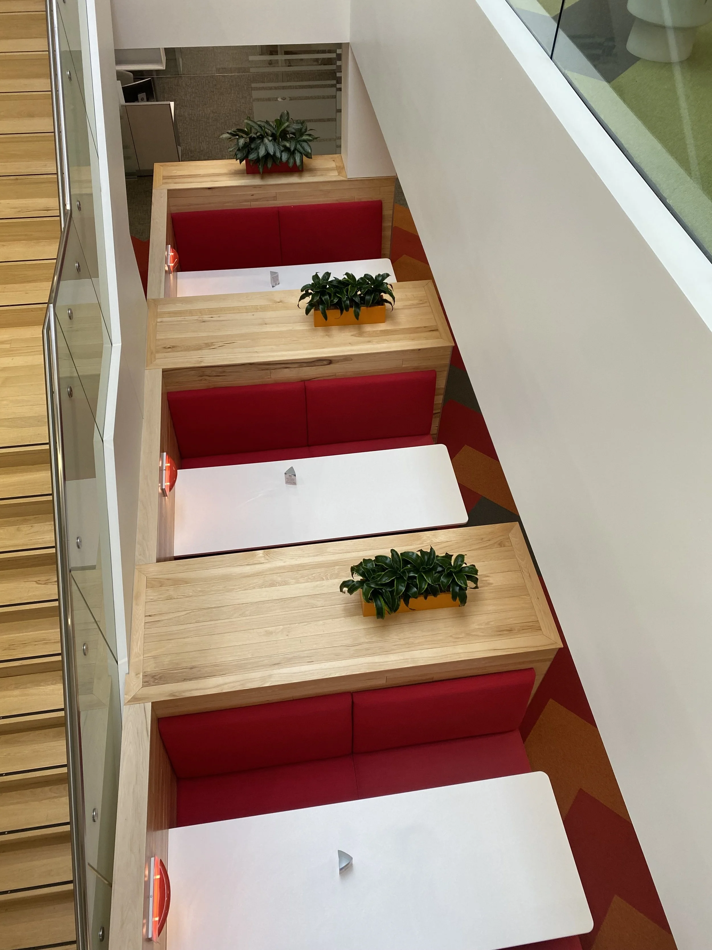 Potted plants lining an open stairwell with red booth seating.
