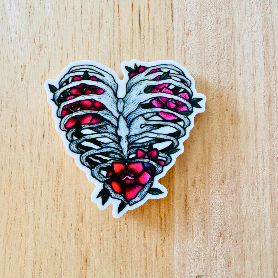 Close-up of the "Love in Bloom" badge reel with a ribcage heart and pink roses design on a rustic wooden backdrop.