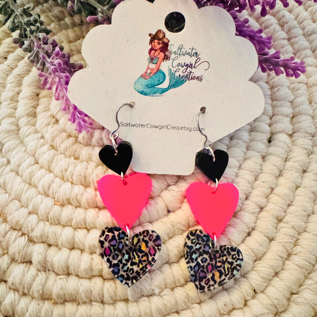Fierce Love Earrings displayed with a lavender accent backdrop, highlighting the trio of vibrant heart shapes.