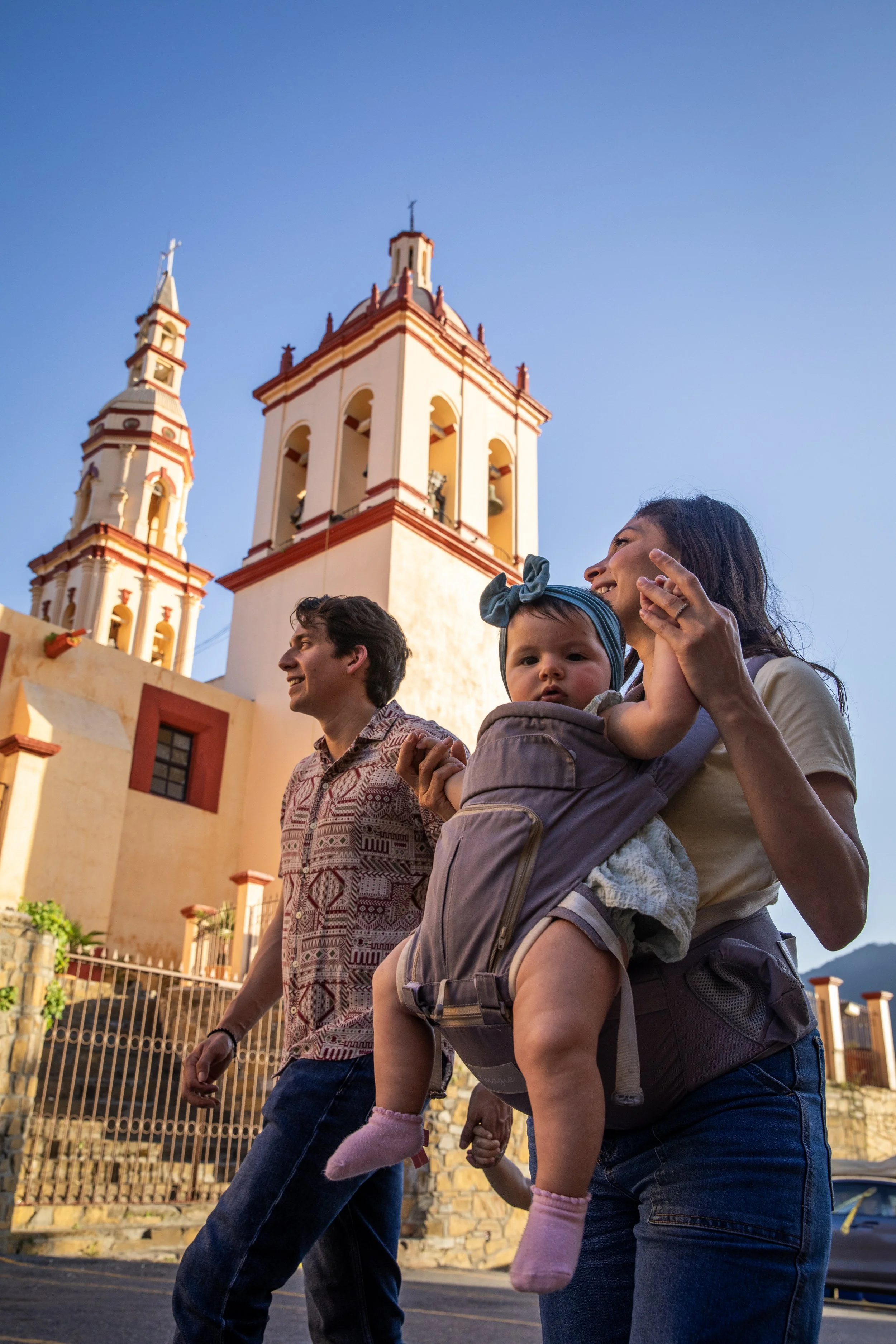 Fotografía Corporativa para Commercial y Publicidad, San Pedro Garza García, México:  Familia paseando en la calle cerca de una iglesia con torres altas, al atardecer, con céu despejado.