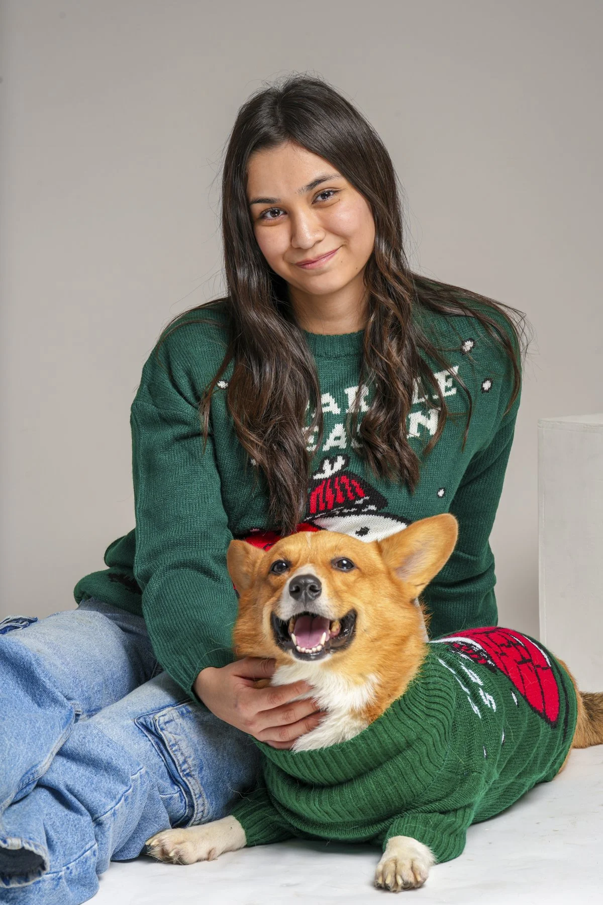 Fotografía de Mascotas: Una joven con sweatshirt verde y un perro Corgi con suéter navideño, ambos sonrientes.