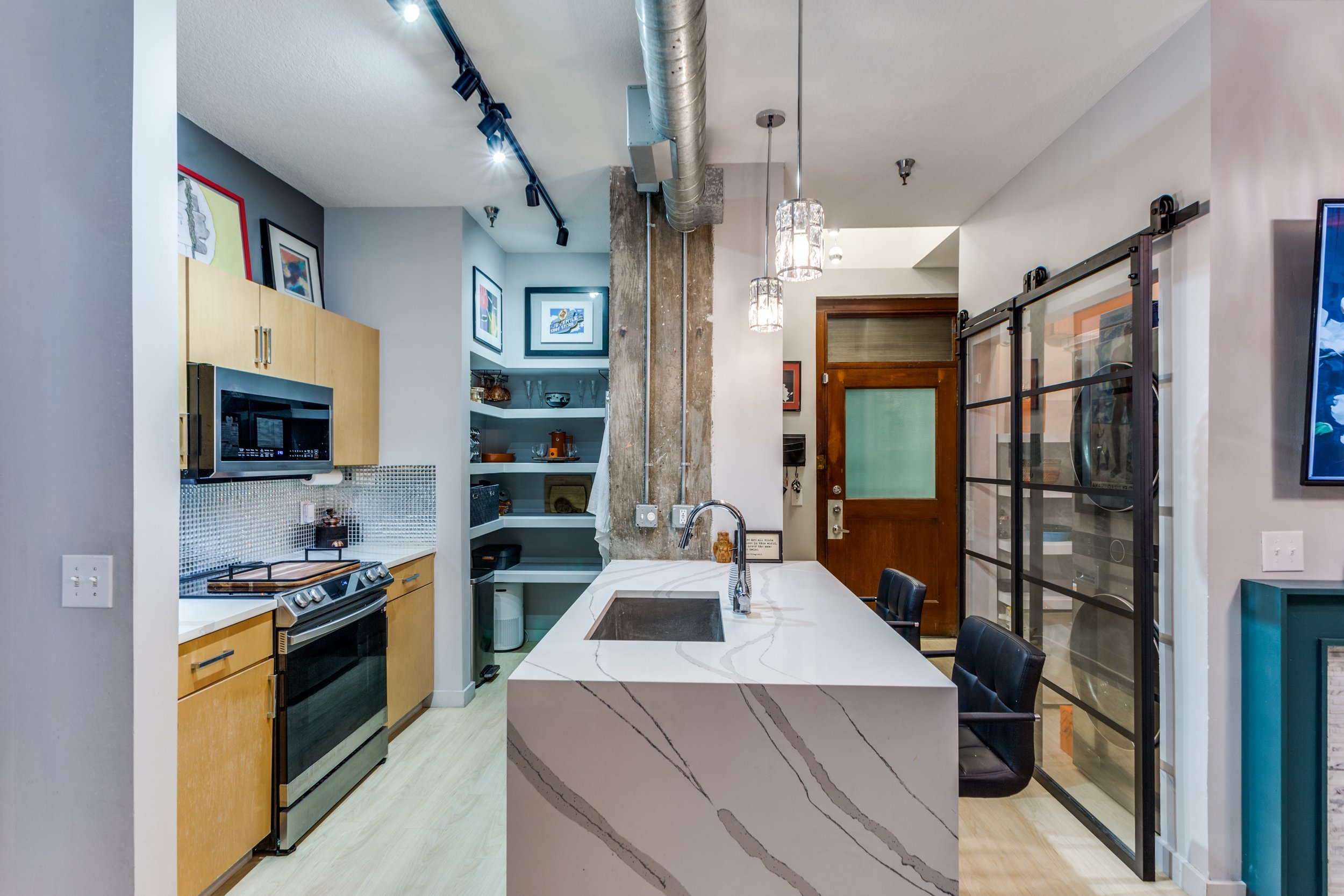 Modern kitchen with white marble island, black chairs, wooden cabinets, and decorative framed art on the walls.