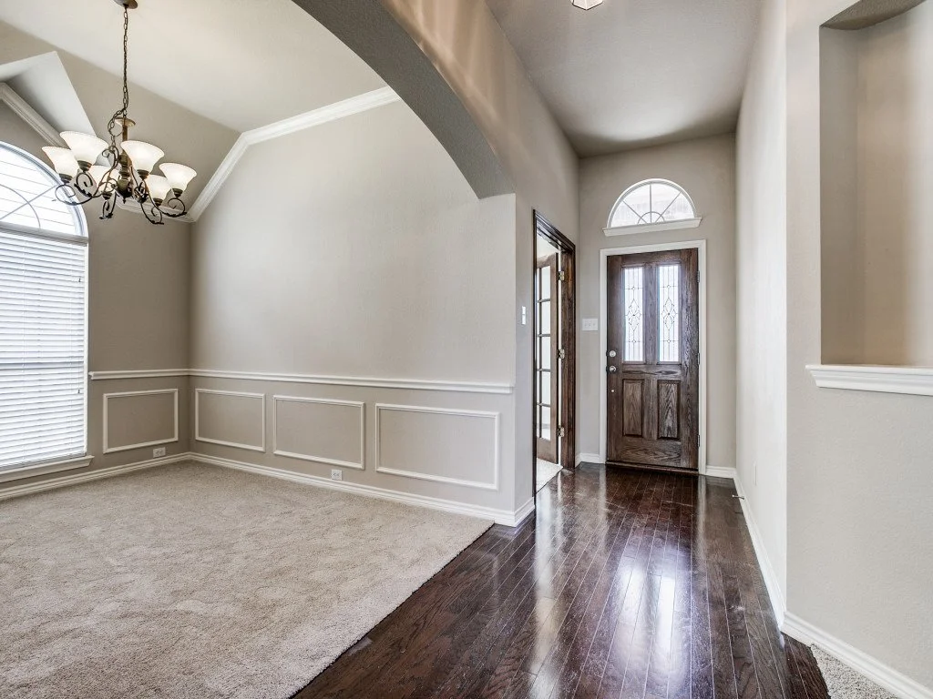 Interior view of a house foyer with a front door, arched windows, hardwood flooring, and a chandelier.