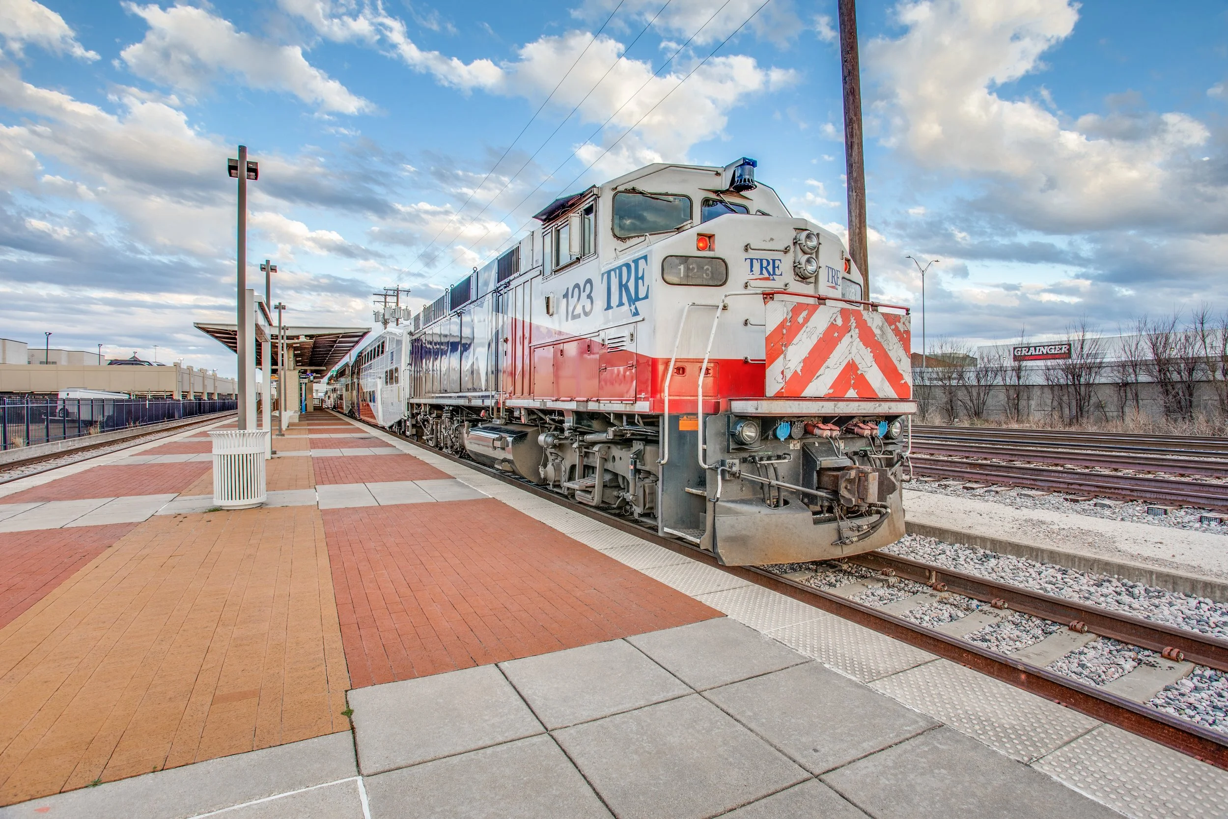 A train stopped at a station platform with a partly cloudy sky in the background.