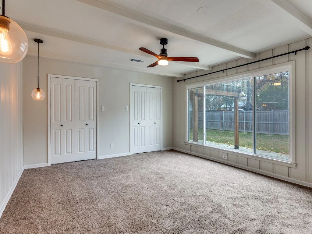 Empty living room with large window, ceiling fan, and pendant lights.