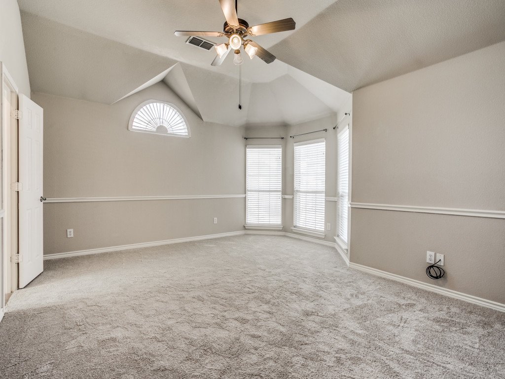 Empty bedroom with beige carpet, three windows with white blinds, a ceiling fan, and an arched window with a semi-circular fanlight.