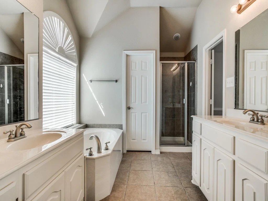 Bathroom with double sinks, bathtub, and glass-enclosed shower.