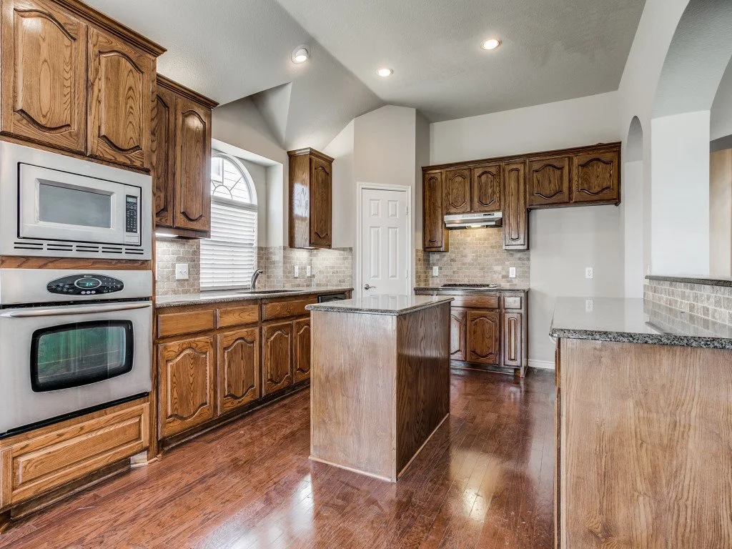 Kitchen with wooden cabinets, granite countertops, stainless steel appliances, and hardwood floors.